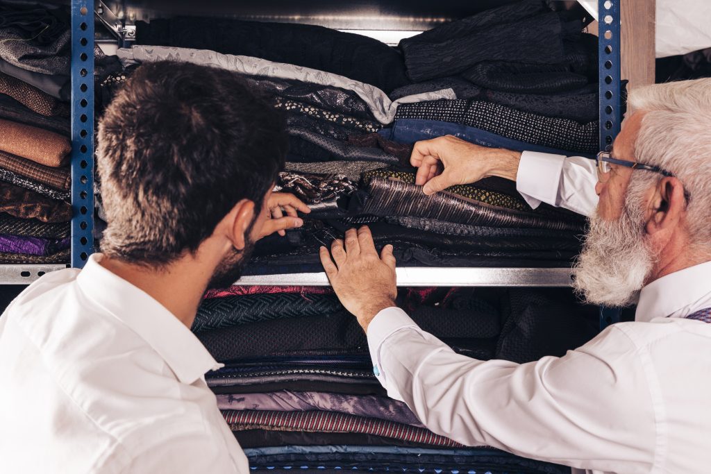 Senior tailor and assistant selecting fabric samples from shelf