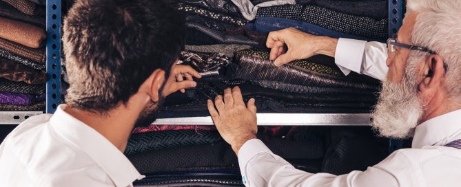 Senior tailor and assistant selecting fabric samples from shelf
